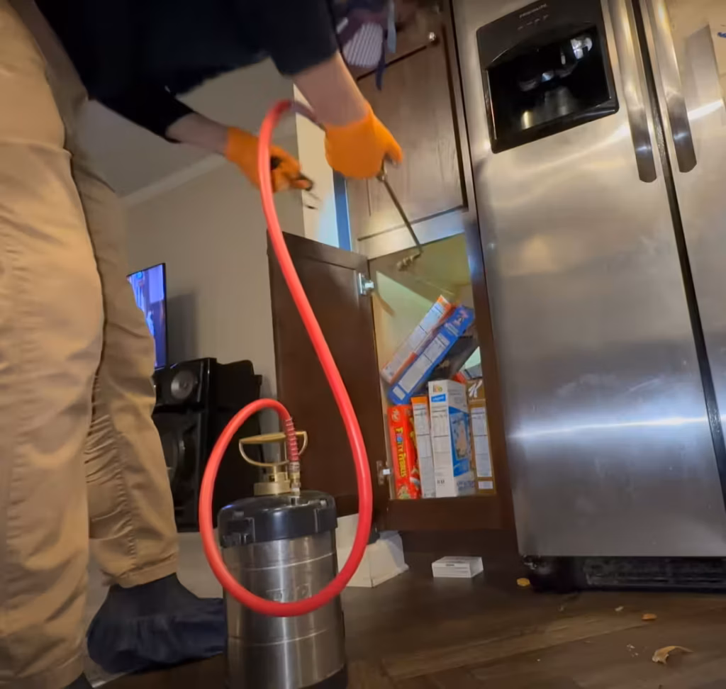 Technician applying pest control services in Phenix City kitchen cabinet.