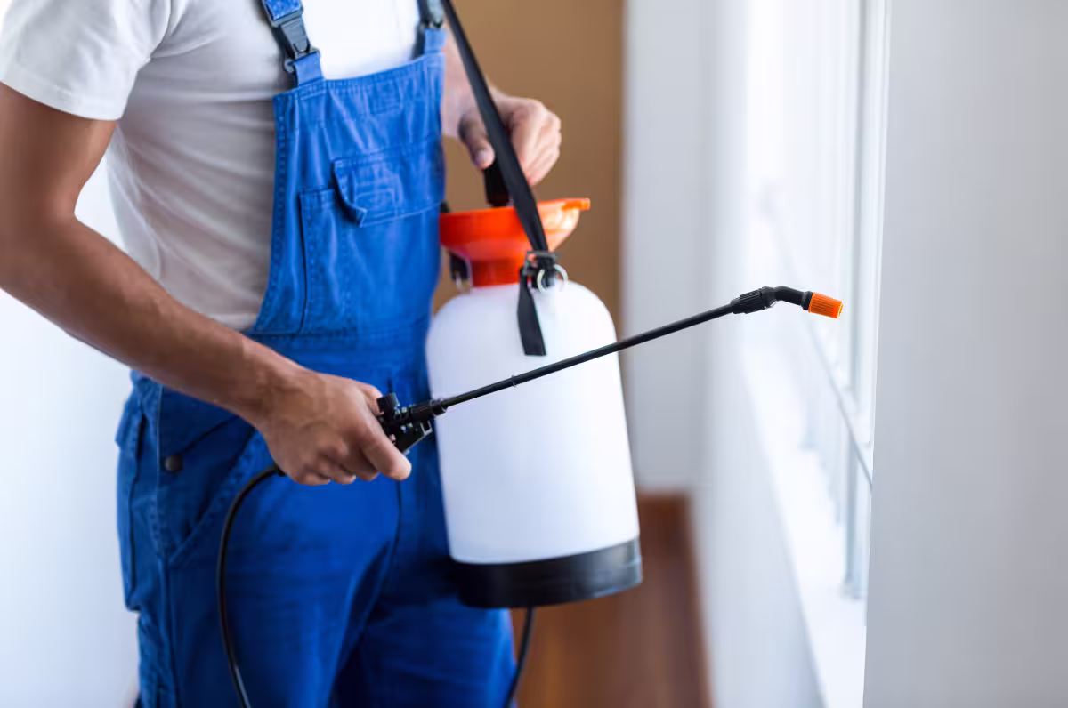 Technician performing Residential Pest Control in Phenix City using a handheld sprayer near a window.